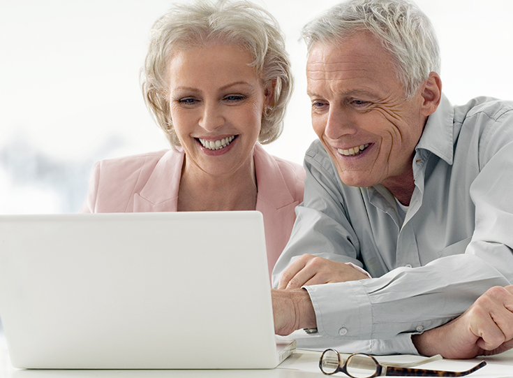 Senior couple smiling as they read on their laptop together. Senior couple smiling as they read on their laptop together.