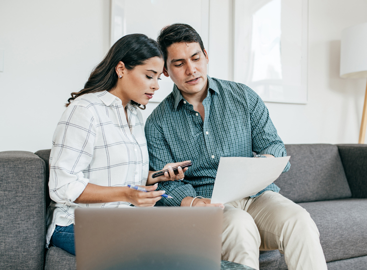 A woman and man review paperwork while sitting on a couch A woman and man review paperwork while sitting on a couch