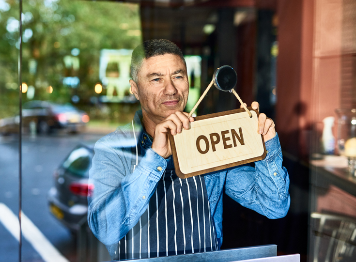Business owner positions an "open" sign in a window Business owner positions an "open" sign in a window