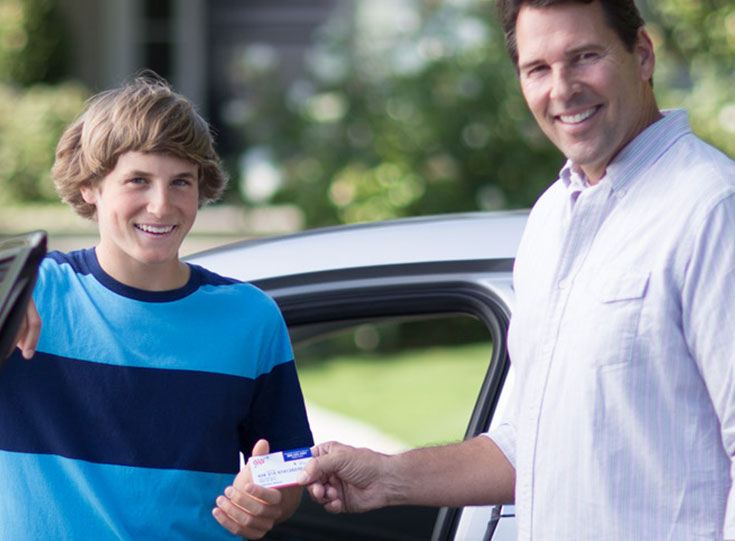 Father handing son AAA card by car Father handing son AAA card by car