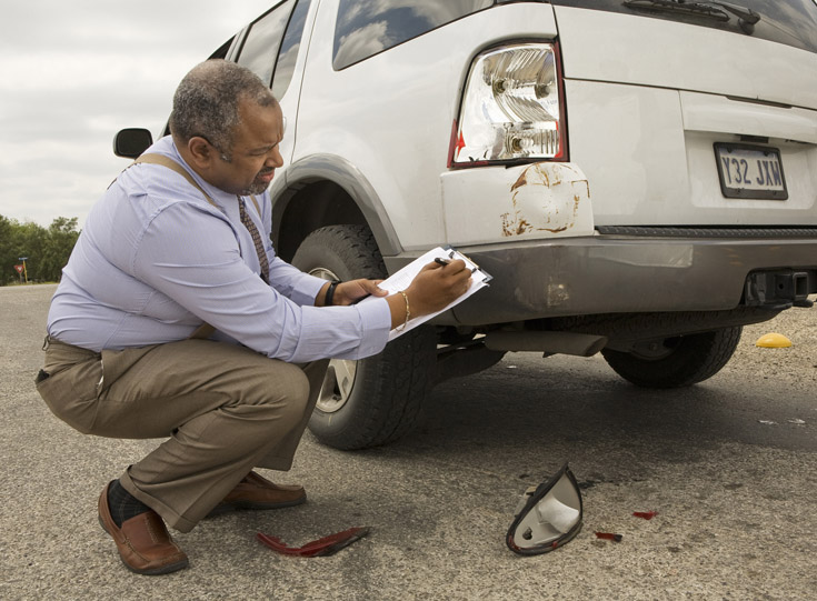 Claims agent taking notes while inspecting a damaged vehicle Claims agent taking notes while inspecting a damaged vehicle