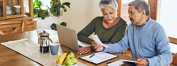 An older couple working through financial documents on a laptop An older couple working through financial documents on a laptop