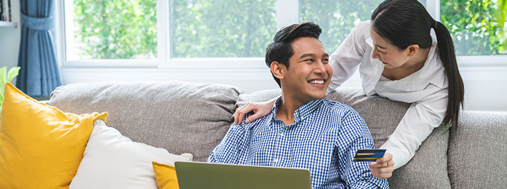 A young couple on the couch in the living room shopping online with a laptop and credit card. A young couple on the couch in the living room shopping online with a laptop and credit card.