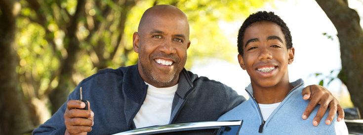 Father holding up car key with arm around son Father holding up car key with arm around son