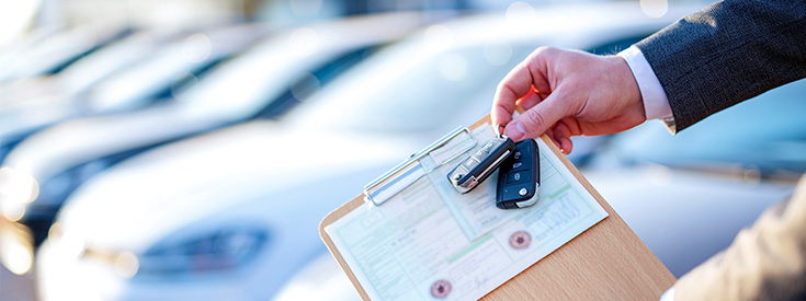A car salesperson holding a clipboard with car keys at the dealership A car salesperson holding a clipboard with car keys at the dealership