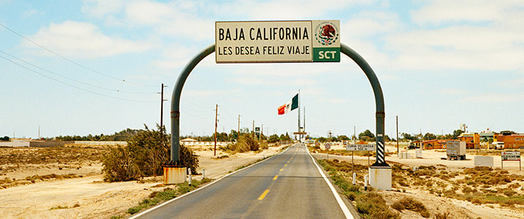 Baja California sign over a roadway, with the Mexican flag in the background Baja California sign over a roadway, with the Mexican flag in the background
