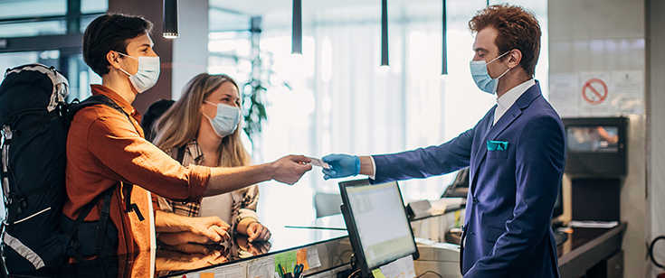 Masked concierge handing card back to masked travelers Masked concierge handing card back to masked travelers