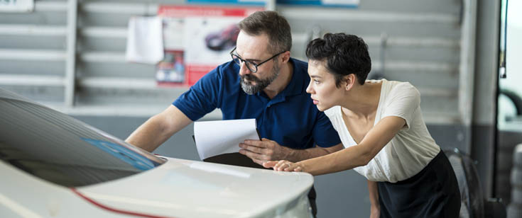 Collision shop employee looking at repairs with car owner Collision shop employee looking at repairs with car owner