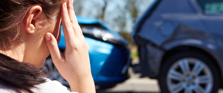 Woman holding hand to head looking at car accident Woman holding hand to head looking at car accident