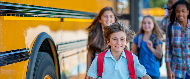 Boy running near school bus as girls walk behind him. Boy running near school bus as girls walk behind him.