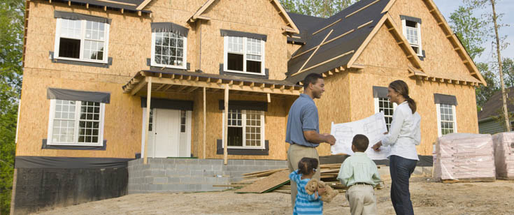 Family of 4 looking at blueprint outside of home under construction Family of 4 looking at blueprint outside of home under construction