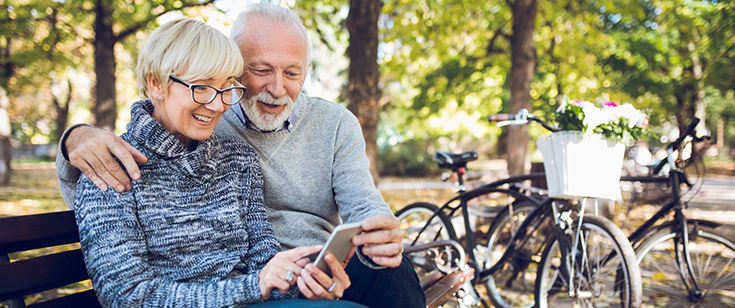 Senior couple looking at cell phone on bench Senior couple looking at cell phone on bench
