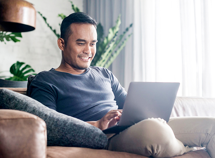 Smiling man works on laptop while sitting on couch Smiling man works on laptop while sitting on couch