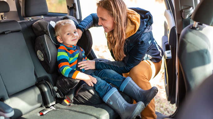 Mother securing a young child into a car seat.