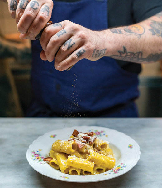 Pepper being ground over a plate of rigatoni alla carbonara.