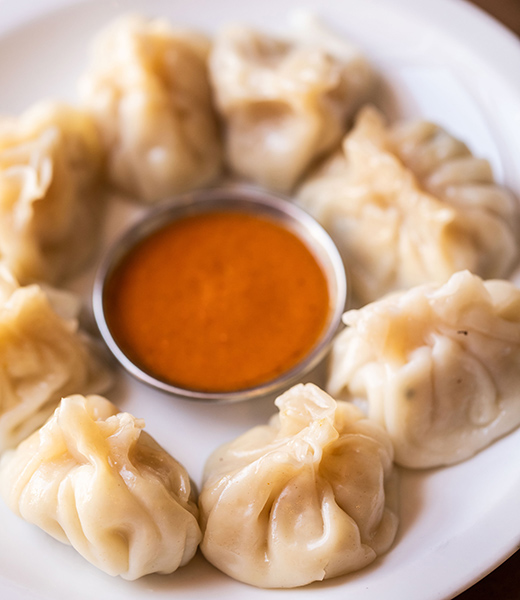 A ring of momos surround a serving of dipping sauce in the center