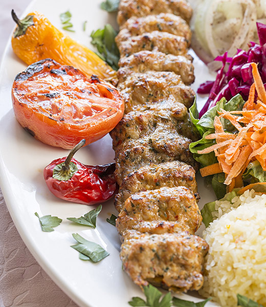 A plate with kebab, roasted veggies, and other sides at Chicken Adana