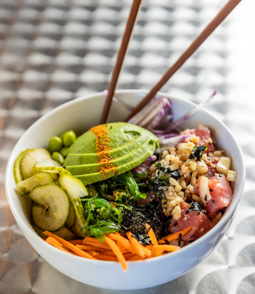 Poke bowl with toppings including avocado, seaweed salad, sliced carrots, and more