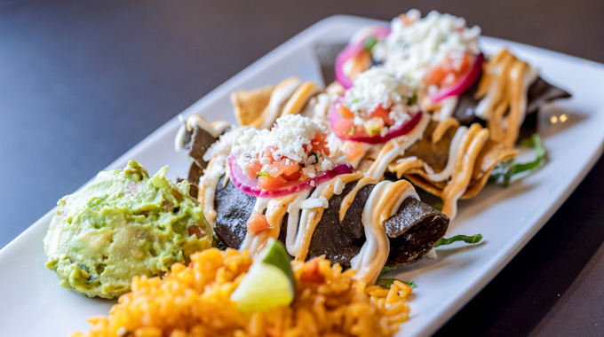 A trio of tacos served with a scoop of guacamole and rice