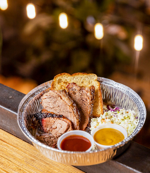 A BBQ plate with slices of meat, cornbread, and a scoop of coleslaw