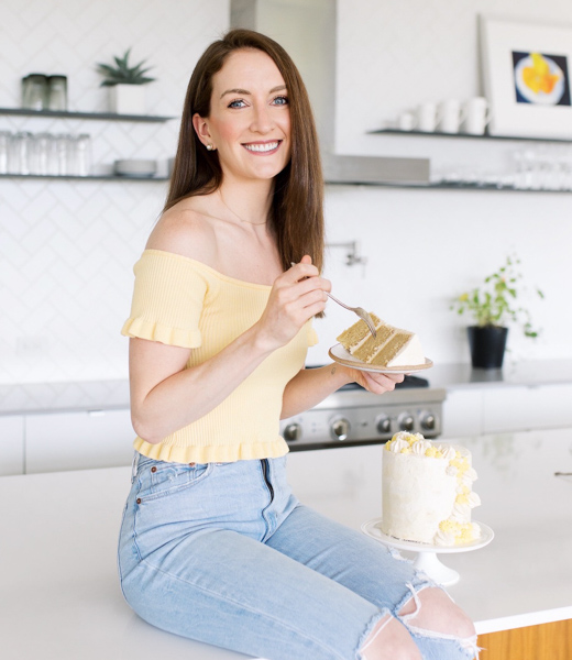 Claire Cary holding a slice of cake while seated on a kitchen counter