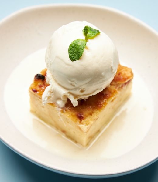 A slice of bread pudding topped with a generous scoop of vanilla ice cream