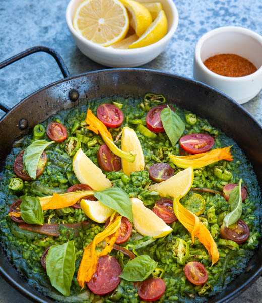 A pan of arroz verde with cherry tomatoes, summer squash, shishito peppers, and basil