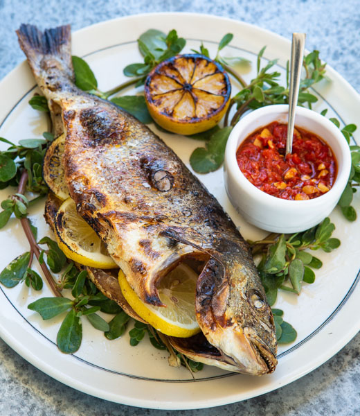 Roasted sea bream arranged over a bed of herbs with lemon slices 