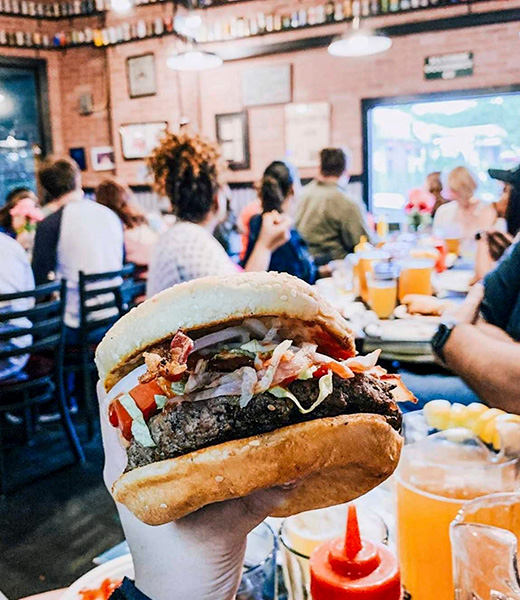 Someone holding up a burger at Westport Flea Market Bar & Grill