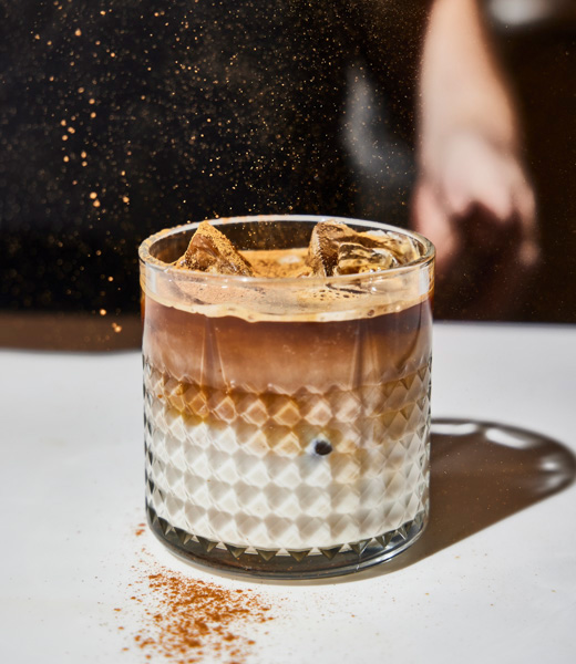 Cinnamon being sprinkled over a glass of iced coffee.