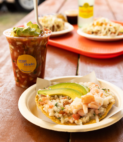 Servings of shrimp cocktail and ceviche tostada, both topped with avocado.