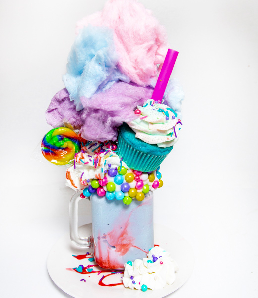 A milkshake piled high with candy-studded whipped cream, cotton candy, and a cupcake