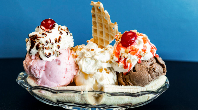 A banana split with 3 scoops of ice cream, whipped cream, maraschino cherries, and a piece of waffle cone