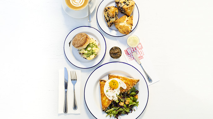 A table with plates holding scones, a breakfast sandwich, and a croque madame