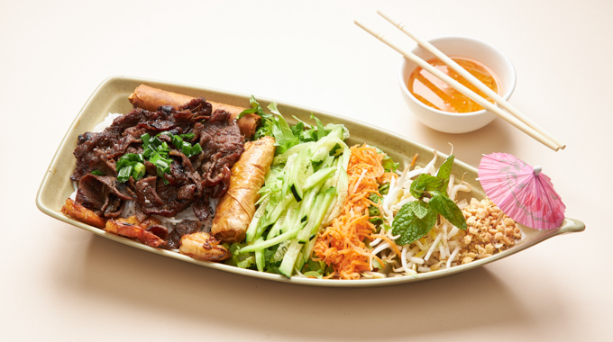 Vermicelli Boat with grilled meat and shrimp, egg rolls, sliced veggies, and peanuts over a bed of noodles