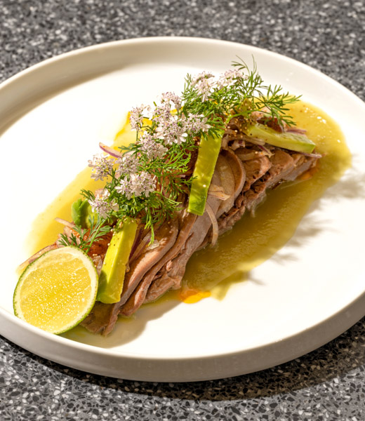 Beef tongue slices topped with avocado and greens