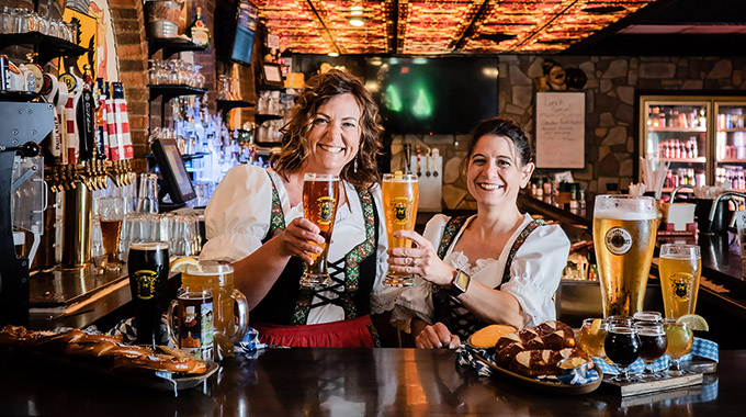 A pair of dirndl-clad women hold up glasses of beer at Schnitzelbank 