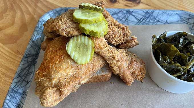 Fried chicken topped with pickles and a side of collard greens at Grace Meat + Three