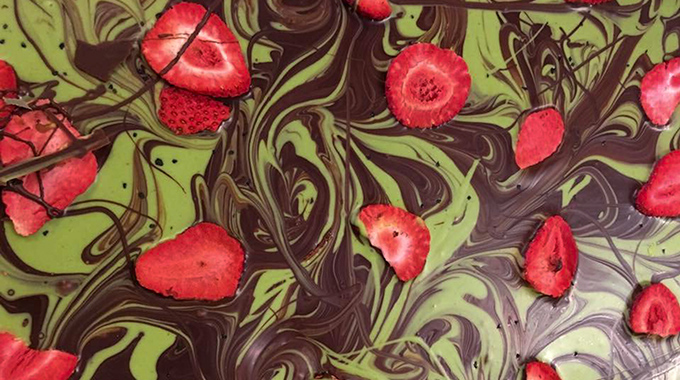 A bar of swirled dark chocolate, matcha, and strawberry slices