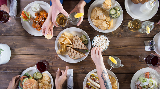 Diners sharing a spread of sandwiches, chips, wings, and more