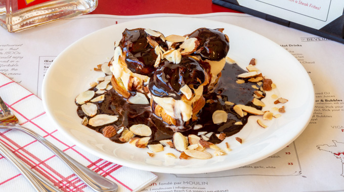 A plate of 3 profiteroles topped with chocolate, ice cream, and almonds