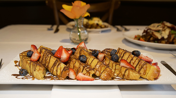 Slices of brioche French toast topped with berries and drizzled in sauce
