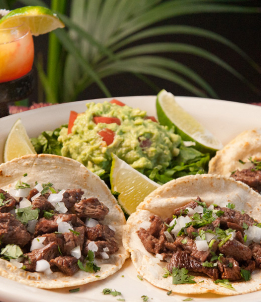 A plate of tacos, guacamole, and lime slices