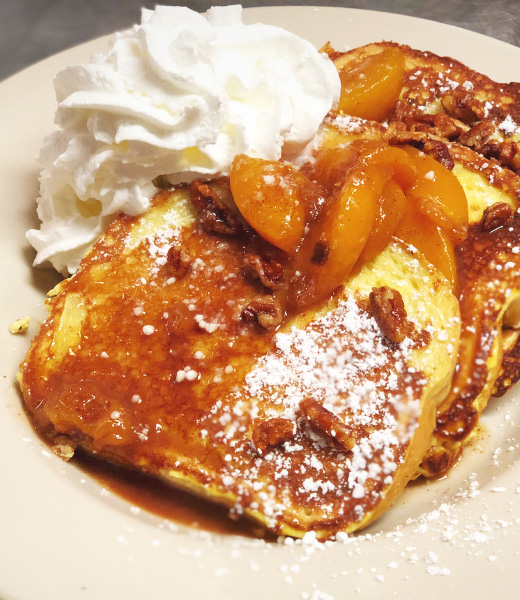 French toast topped with peach slices, powdered sugar, and whipped cream