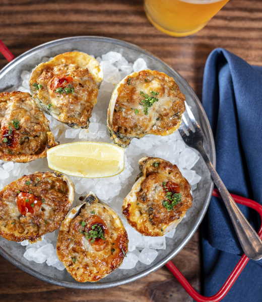 Chef Brue's oysters Pacific is a sassy riff on oysters Rockefeller, baked with house-made chorizo sausage, locally grown cherry tomato, and shaved Manchego cheese.