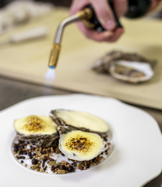 Chef Brust takes a flame to his oysters Rockefeller to caramelize a freshly whipped lemon sabayon topping, making for a decadent dish.