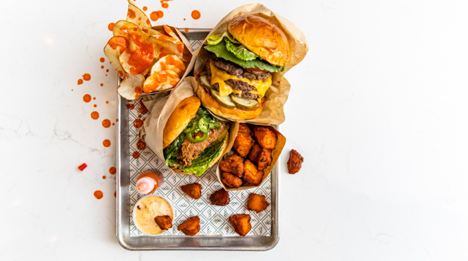 A couple of burgers, chips, and crispy sweet potatoes on a paper-lined tray