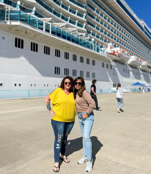 Two women posing in front of a docked cruise ship.