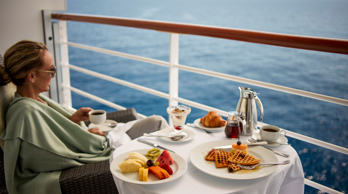 Woman enjoying room service on her stateroom balcony.