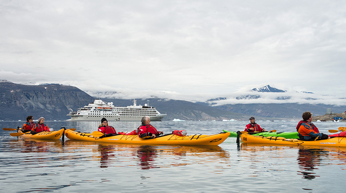 A cruise ship sitting in the distance behind a group of kayakers